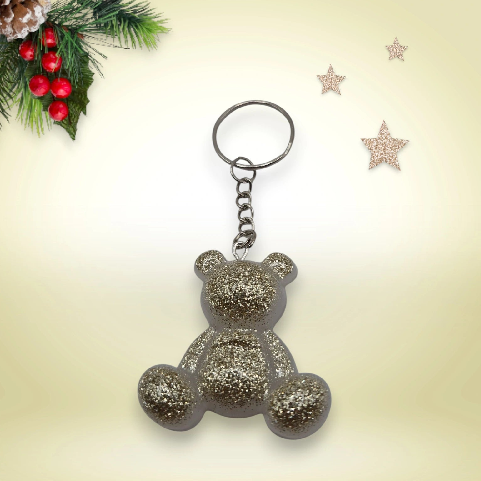 Porte-clés grand ourson en résine blanc doré pailletée nacré, avec anneau argenté, posé sur un fond orné de branches de sapin et d’étoiles décoratives.