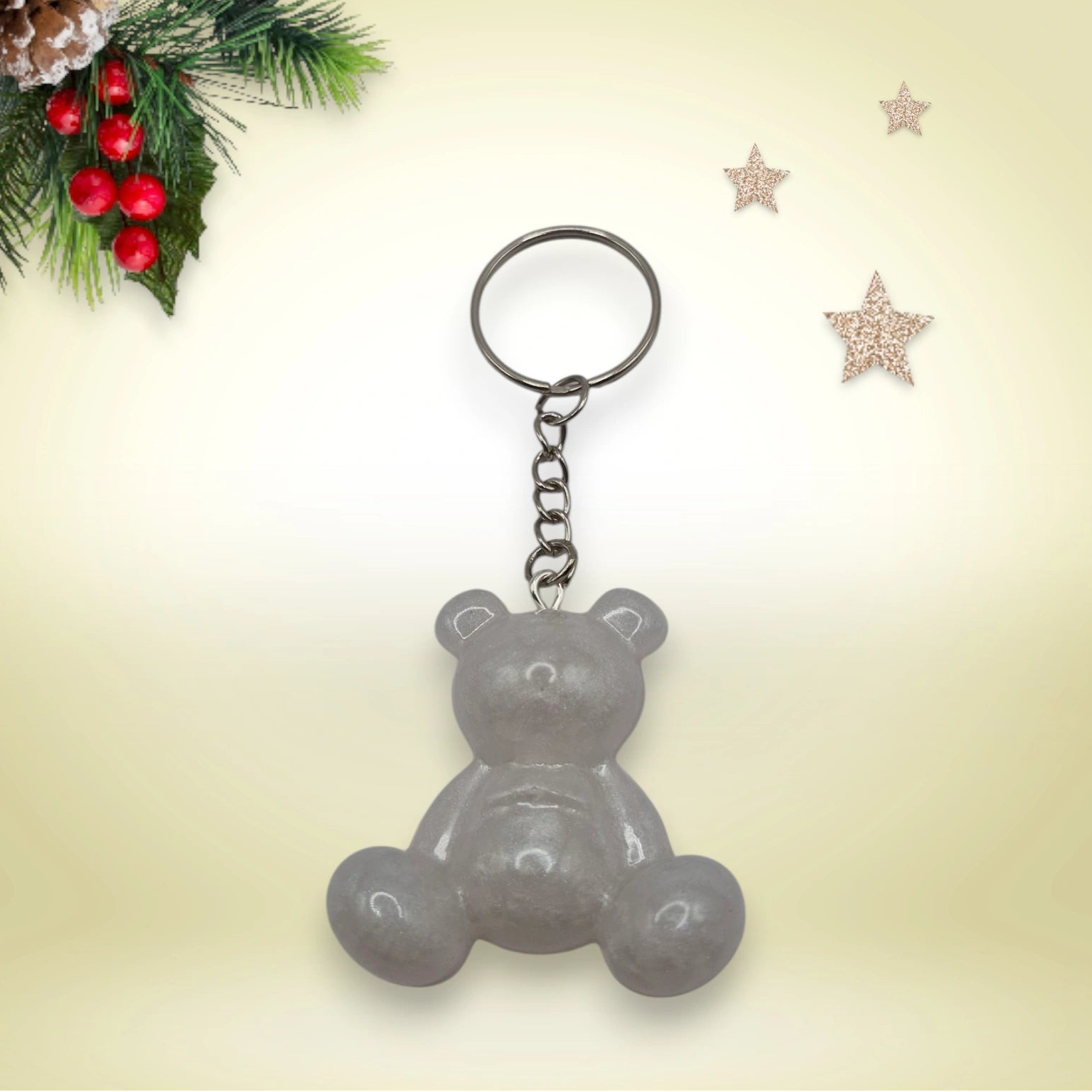 Porte-clés grand ourson en résine blanc nacré, avec anneau argenté, posé sur un fond orné de branches de sapin et d’étoiles décoratives.