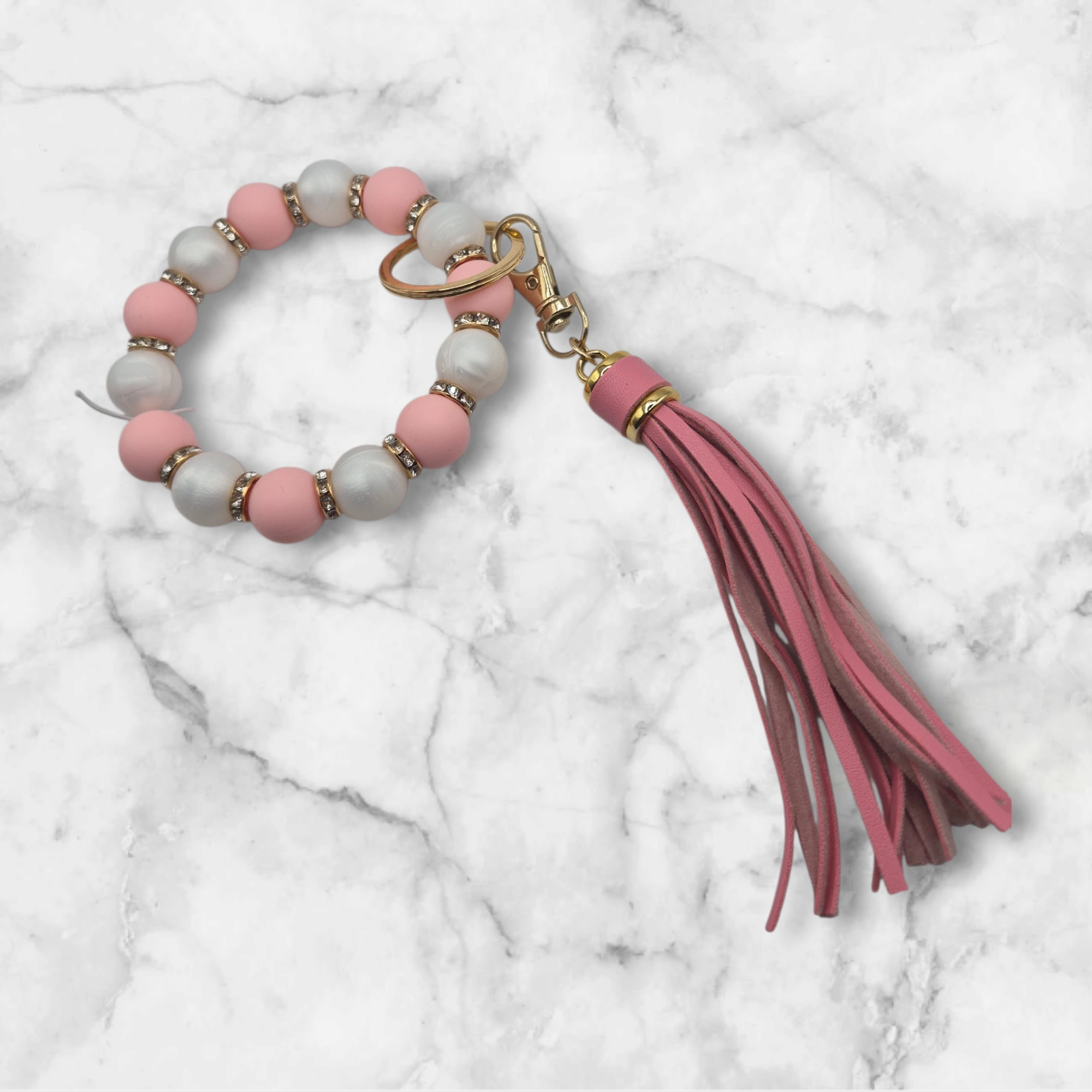 Porte-clé en perles de silicone rose et blanc nacré, agrémenté de perles d'espacement métalliques incrustées de strass. Il est doté d'un anneau brisé et d'un mousqueton dorés, ainsi que d'un pompon décoratif rose vif.