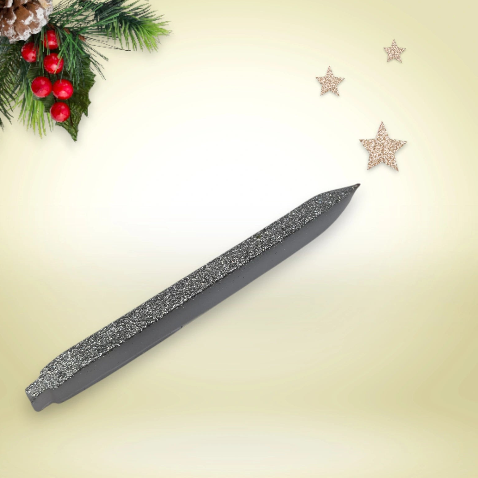 Stylo argent pailleté en résine époxy avec encre noire, présenté sur un décor de Noël composé de branches de pin et d’étoiles festives.