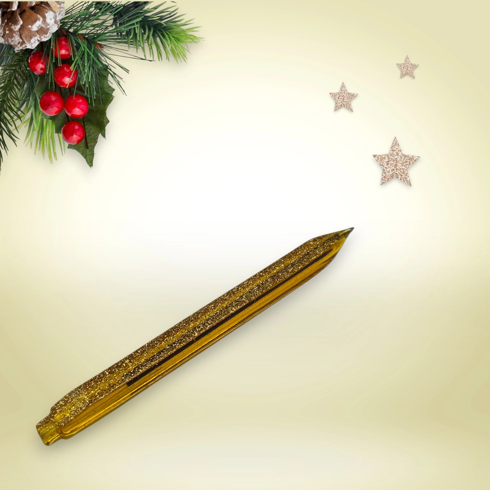 Stylo doré pailleté en résine époxy avec encre noire, présenté sur un décor de Noël composé de branches de pin et d’étoiles festives.