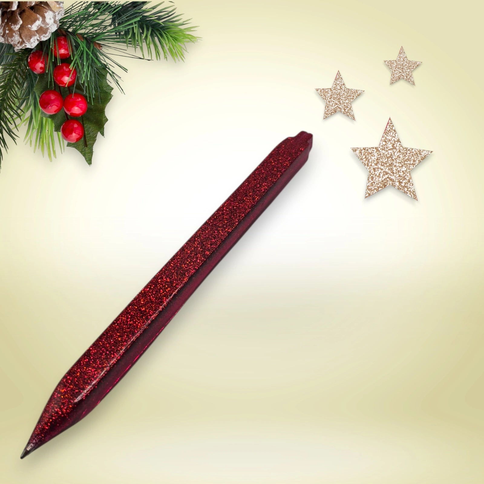 Stylo rouge pailleté en résine époxy avec encre noire, présenté sur un décor de Noël composé de branches de pin et d’étoiles festives.