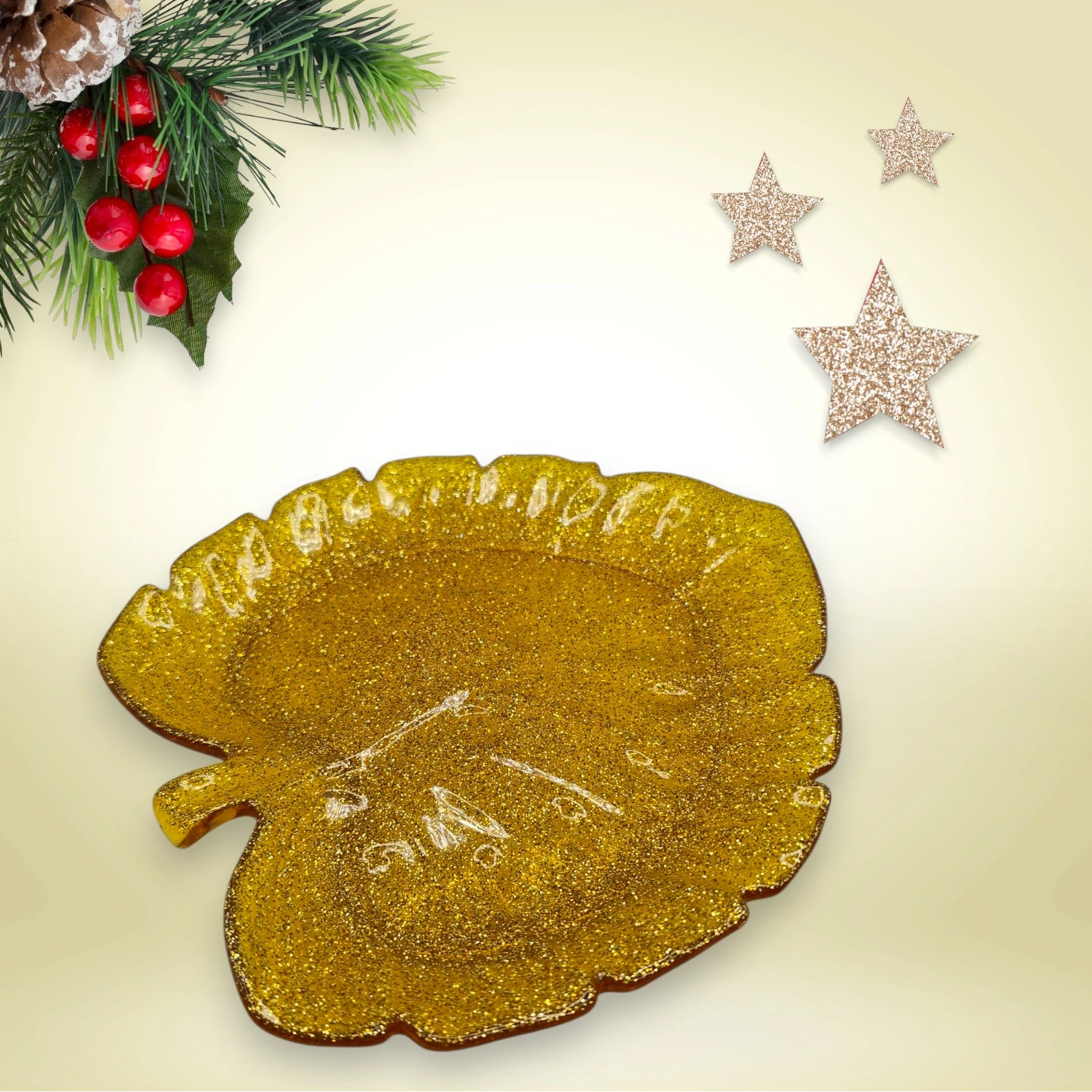 Vide-poche artisanal en résine époxy dorée en forme de feuille, posé sur un fond décoratif avec branches de sapin et étoiles scintillantes