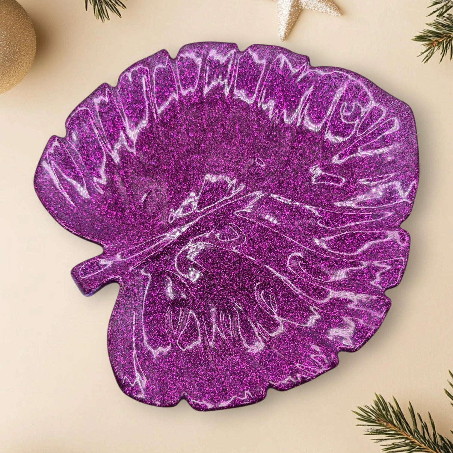 Vide-poche artisanal en résine époxy violet en forme de feuille, posé sur un fond décoratif avec branches de sapin, étoile et boules scintillantes.