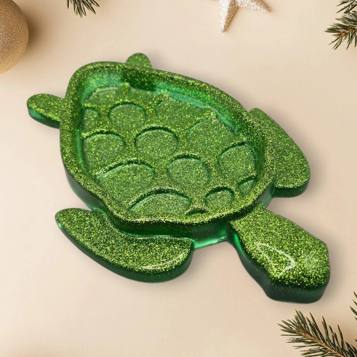 Vide-poche en résine pailletée verte claire, en forme de tortue, décoré d’un fond agrémenté de branches de sapin et d’étoiles scintillantes.